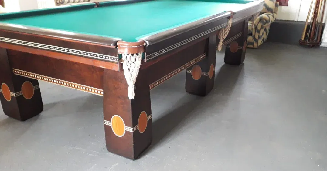 Mesa de bilhar profissional com pano verde, madeira escura entalhada e caçapas com rede.