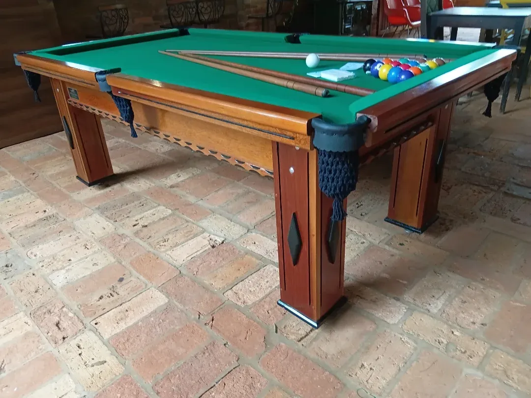 Mesa de ping pong com tampo azul e bordas madeira, capa preta, varanda rústica.