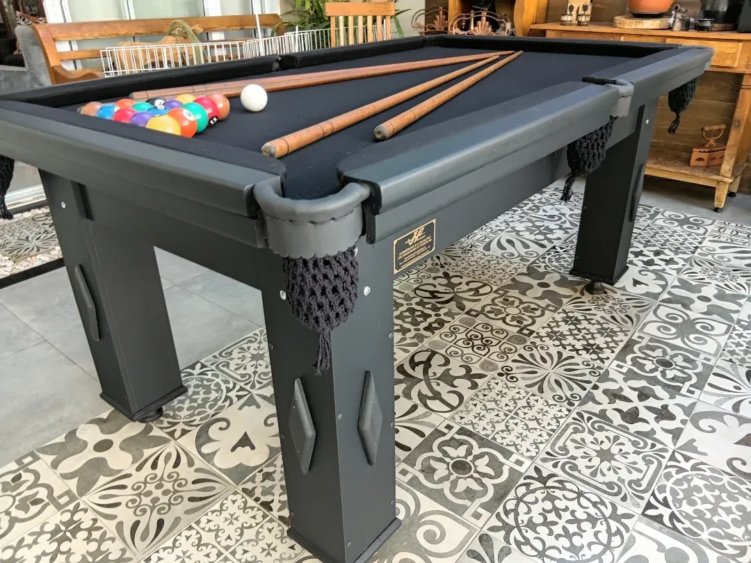 Mesa de bilhar preta com pano preto, bolas coloridas e tacos, piso estampado.