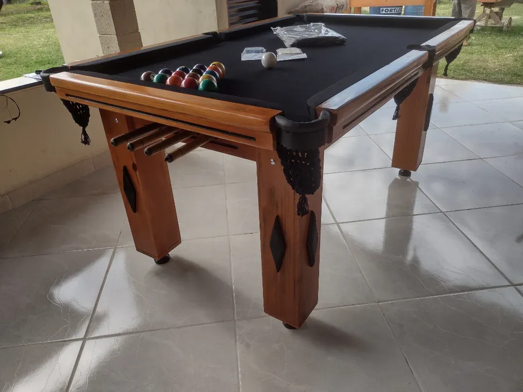 Mesa de bilhar em madeira com pano preto, kit de bolas e acessórios, ambiente interno.