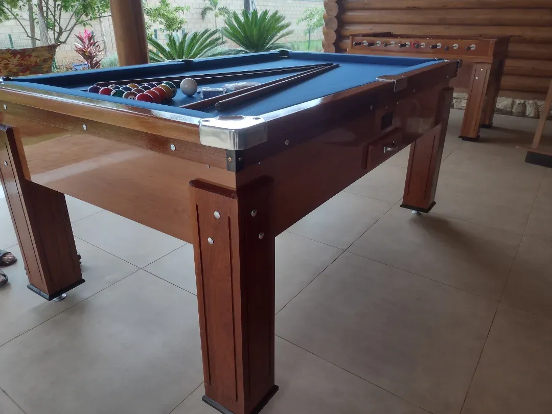 Mesa de sinuca profissional com pano azul e caçapas cromadas, varanda com jardim.