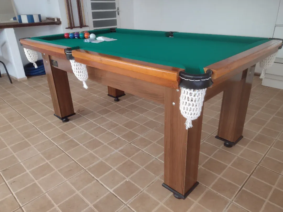 Mesa de sinuca JHP Bilhares com pano verde, caçapas com rede, madeira maciça e bolas ao fundo.