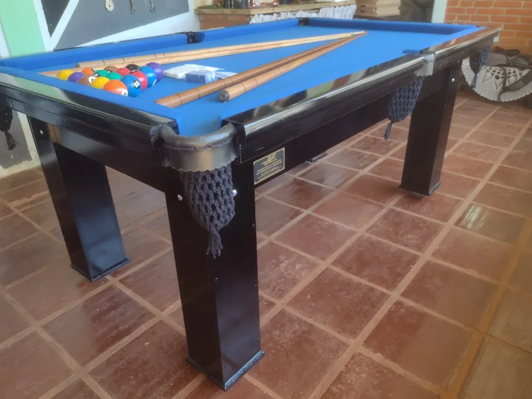 Mesa de bilhar preta com pano azul, caçapas de rede e tacos, acabamento brilhante.