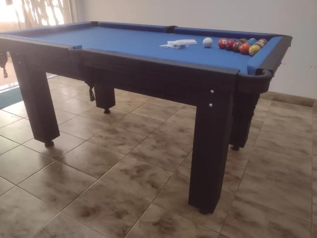 Mesa de sinuca preta com pano azul, caçapas de rede, bolas alinhadas em sala.