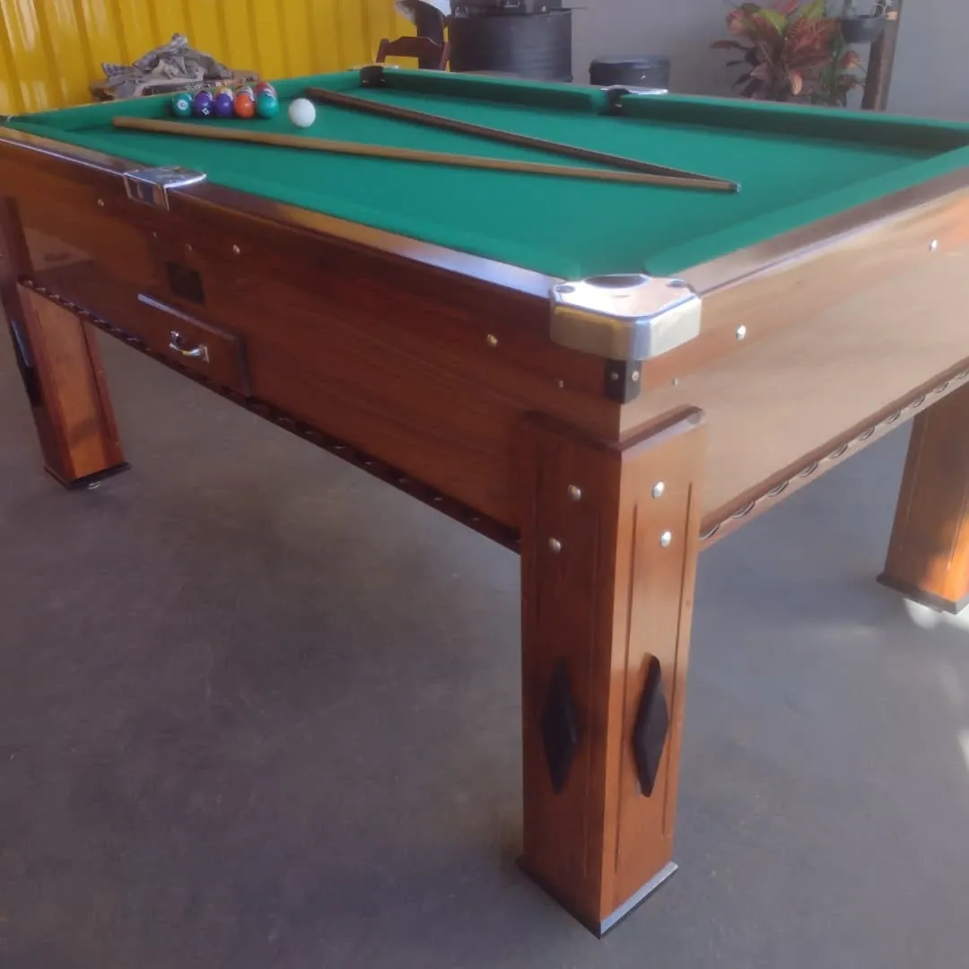 Mesa de bilhar madeira escura com pano verde, bolas e tacos em área externa.